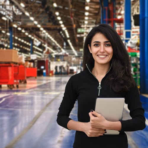 Woman logistician in a black shirt stands on a shiny gray concrete floor in a colorful manufacturing facility holding a notebook