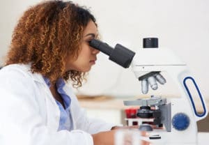 Biology College Major - Woman in white lab coat examines a biological sample under a microscope